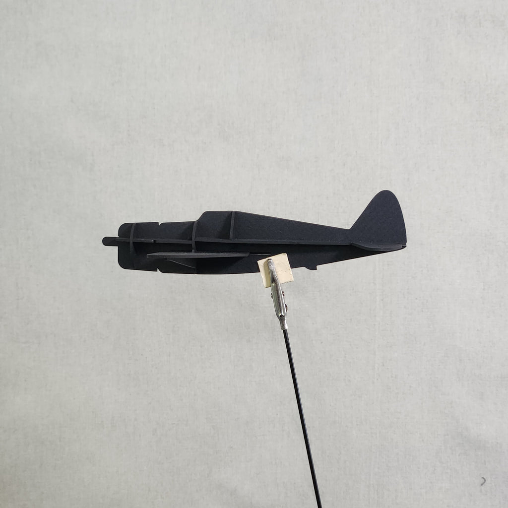 A small black cardboard airplane model of the U.S. Army P-47 Thunderbolt, shown with a metal clip holding a black cable against a light gray textured background.