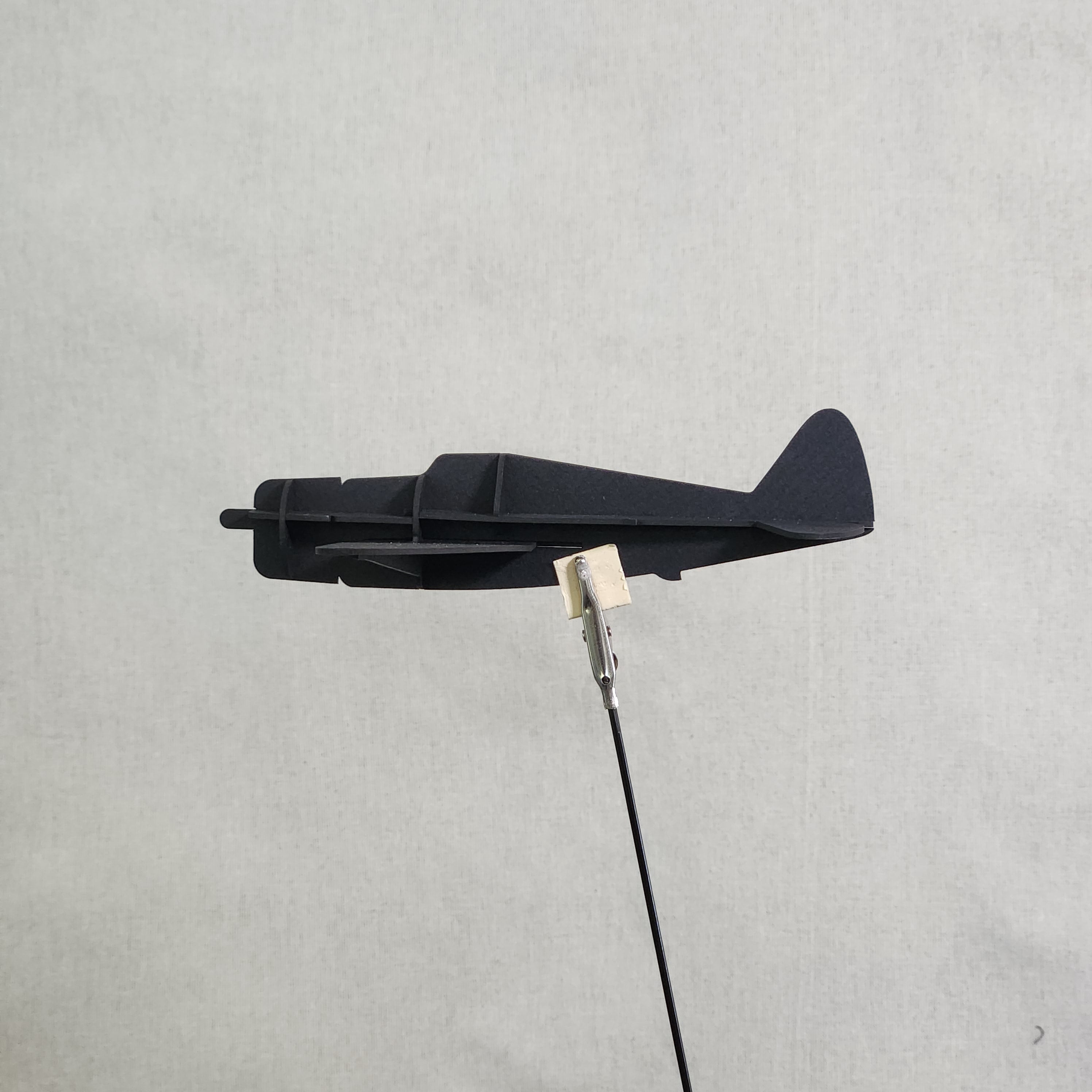 A small black cardboard airplane model of the U.S. Army P-47 Thunderbolt, shown with a metal clip holding a black cable against a light gray textured background.