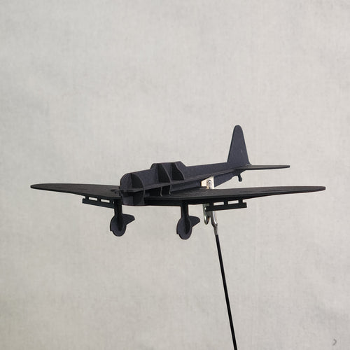 A black cardboard model airplane of the Japanese D3A1 Val, viewed from the underside, mounted on a thin black wire against a light gray background.