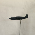 A black cardboard model of a U.S. Army P-51A Mustang airplane assembly attached to a thin black rod with a silver metal clip, shown against a plain light beige background.