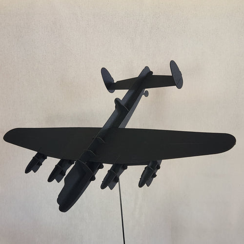 A black cardboard model of a British Lancaster Bomber, a four-engine military aircraft, shown from an overhead perspective against a light beige textured background.